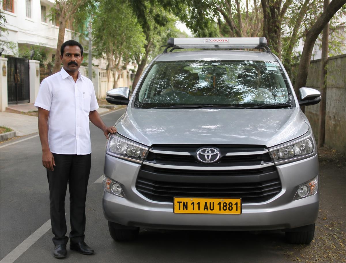 Driver standing beside a clean silver travel vehicle on a Chennai street